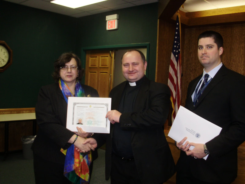 Rev. Boguslaw Janiec standing between a man and woman holding a certificate